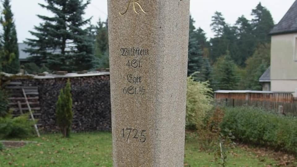 A stone monument with inscriptions, surrounded by grass and trees.