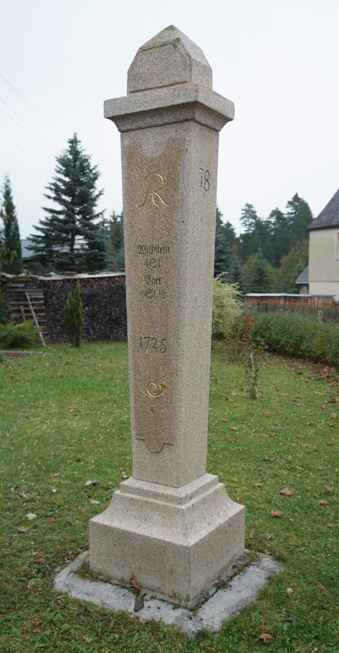 A stone monument with inscriptions, surrounded by grass and trees.