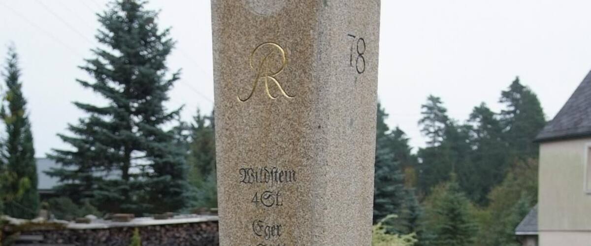 A stone monument with inscriptions, surrounded by grass and trees.