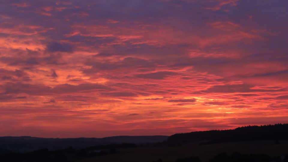 A sunset over a hilly landscape with a vibrant sky.