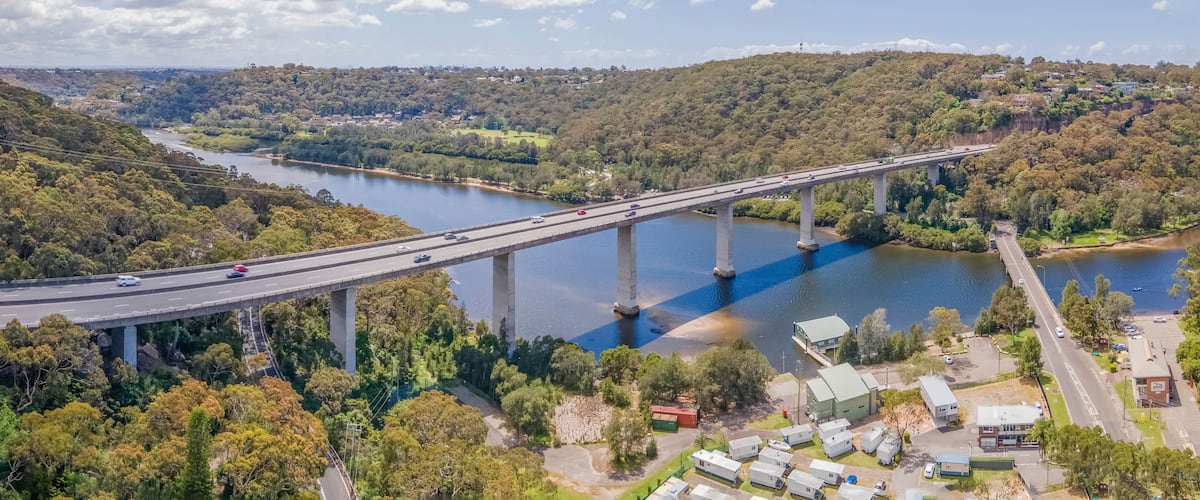 A bridge spanning a river, surrounded by dense forest and residential buildings.