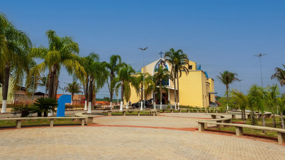 A yellow building with a cross on top, surrounded by palm trees and benches.
