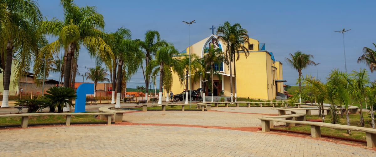 A yellow building with a cross on top, surrounded by palm trees and benches.