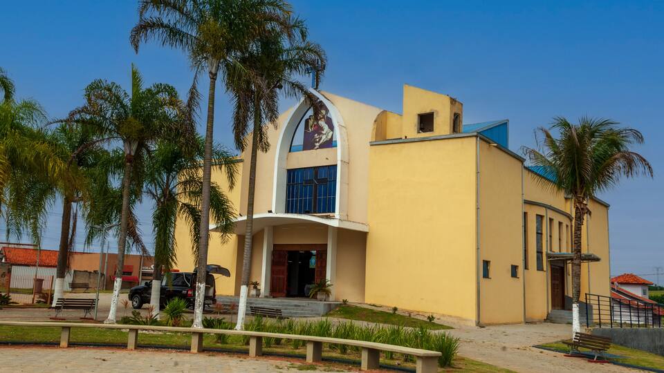 A yellow building with a large arched entrance and palm trees in the foreground.