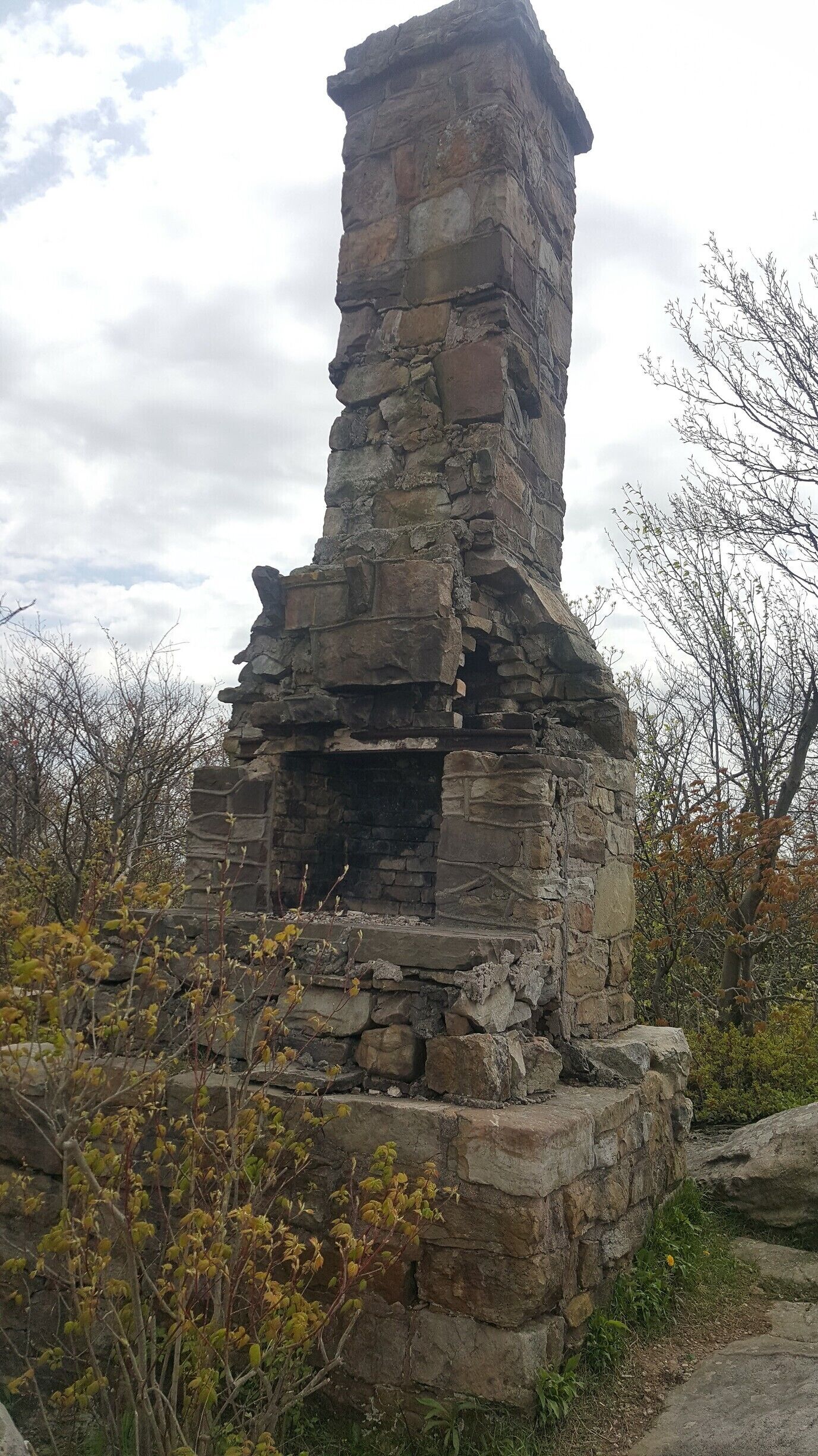 A stone structure with a chimney, surrounded by trees and vegetation.