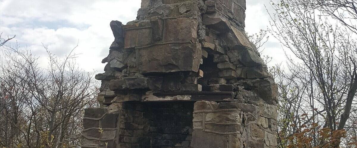 A stone structure with a chimney, surrounded by trees and vegetation.