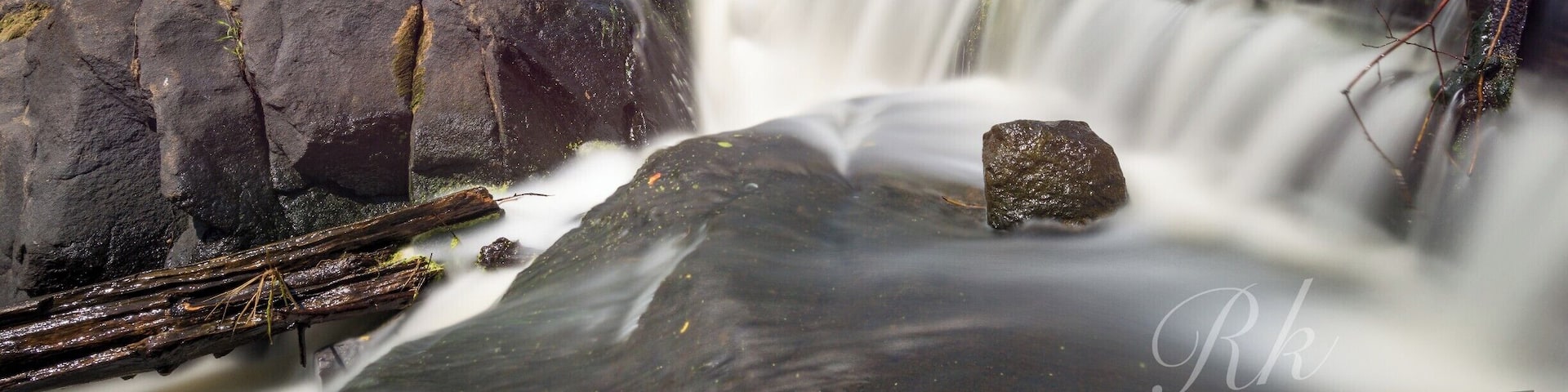 A waterfall cascading over rocks with a forested background and a clear sky.