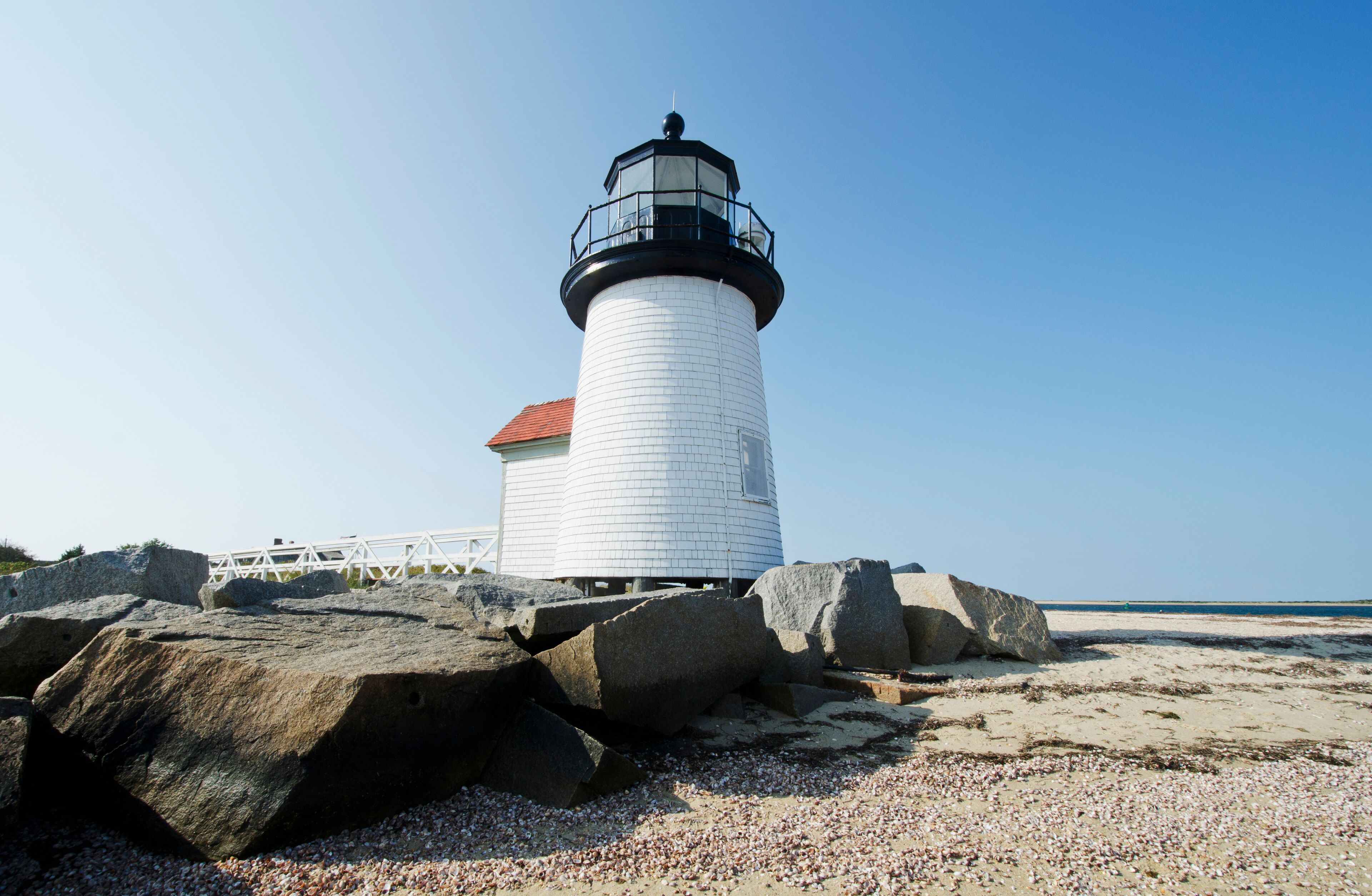 A lighthouse on a rocky beach with a clear blue sky.