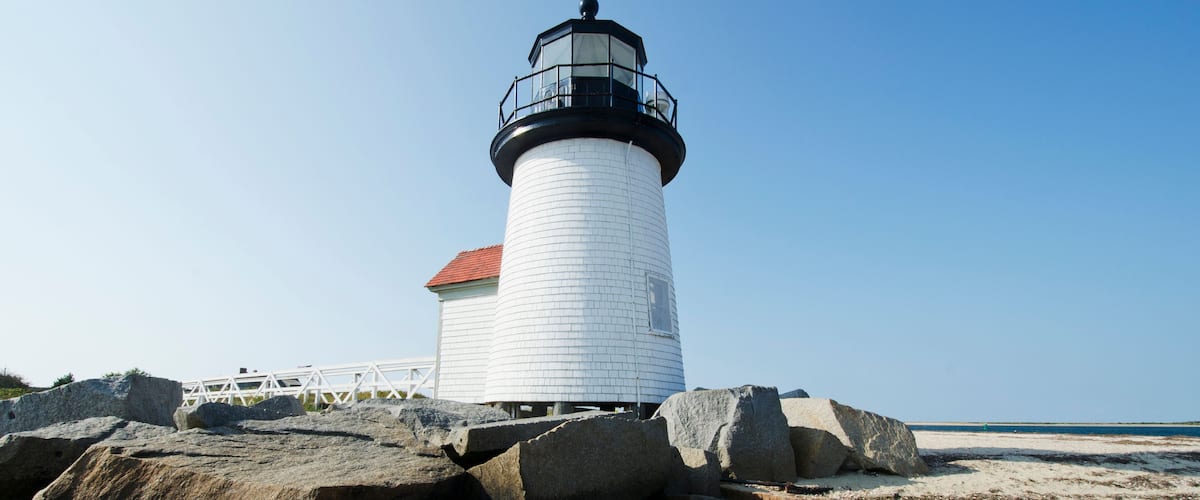 A lighthouse on a rocky beach with a clear blue sky.