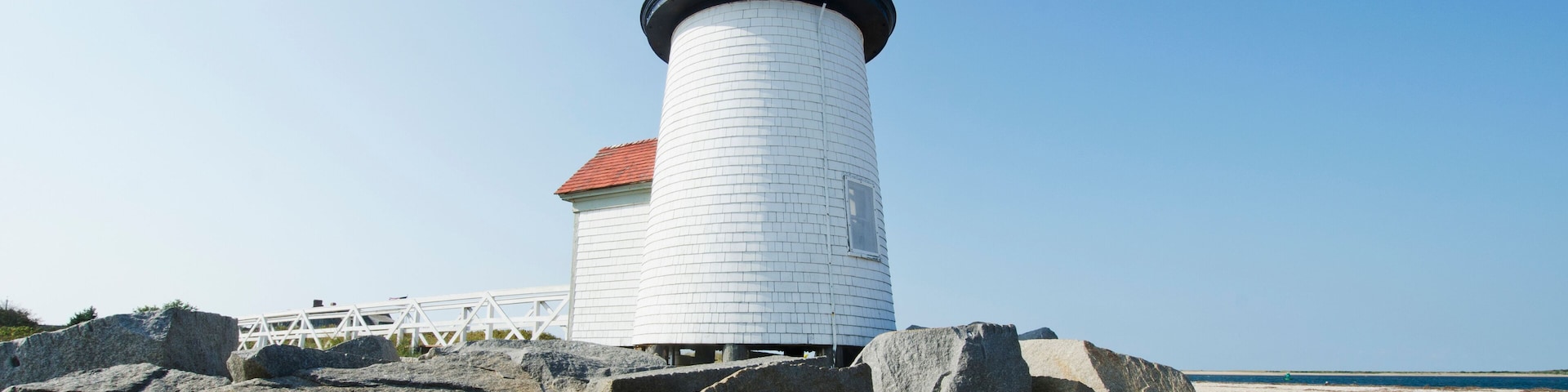 A lighthouse on a rocky beach with a clear blue sky.