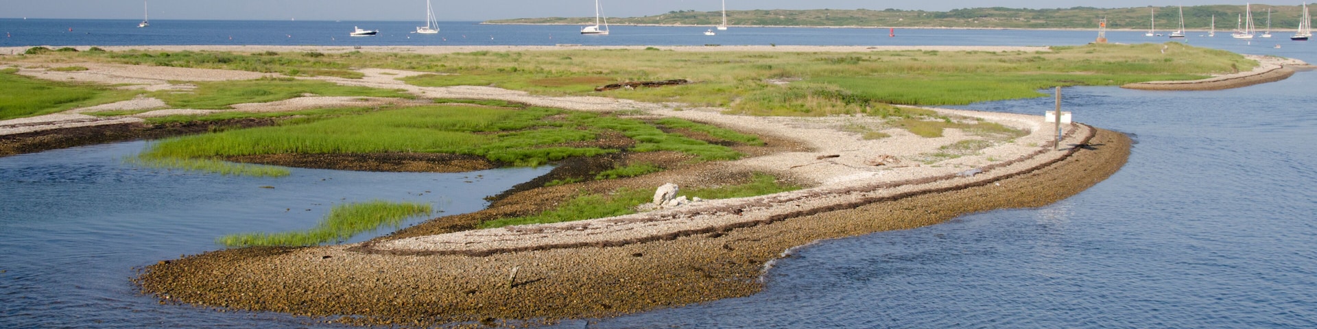 Eine Küstenlandschaft mit Sandstrand, grünen Flächen und einer kleinen Insel mit Leuchtturm.