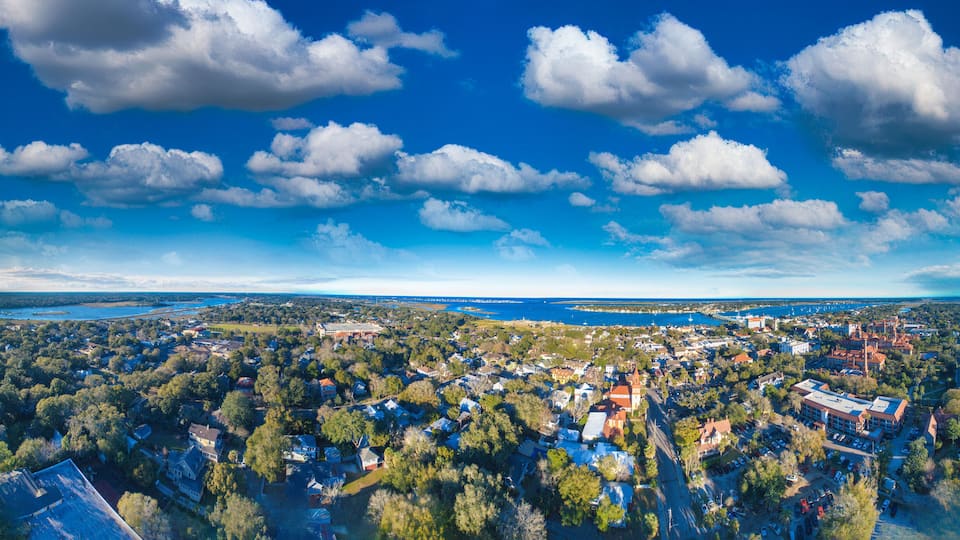 An aerial view of a coastal town with dense residential areas, a prominent church, and a large body of water in the background.