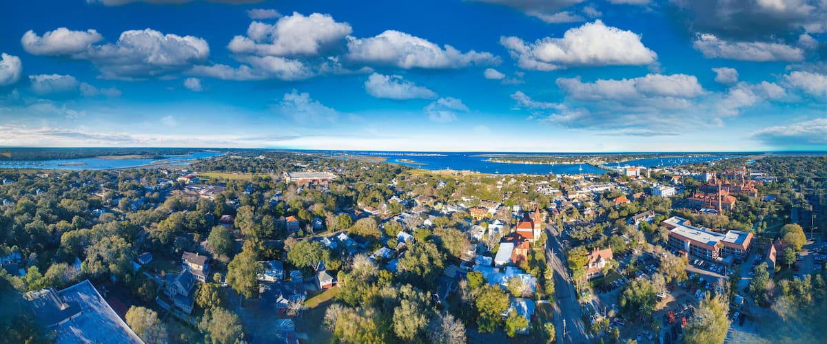 An aerial view of a coastal town with dense residential areas, a prominent church, and a large body of water in the background.
