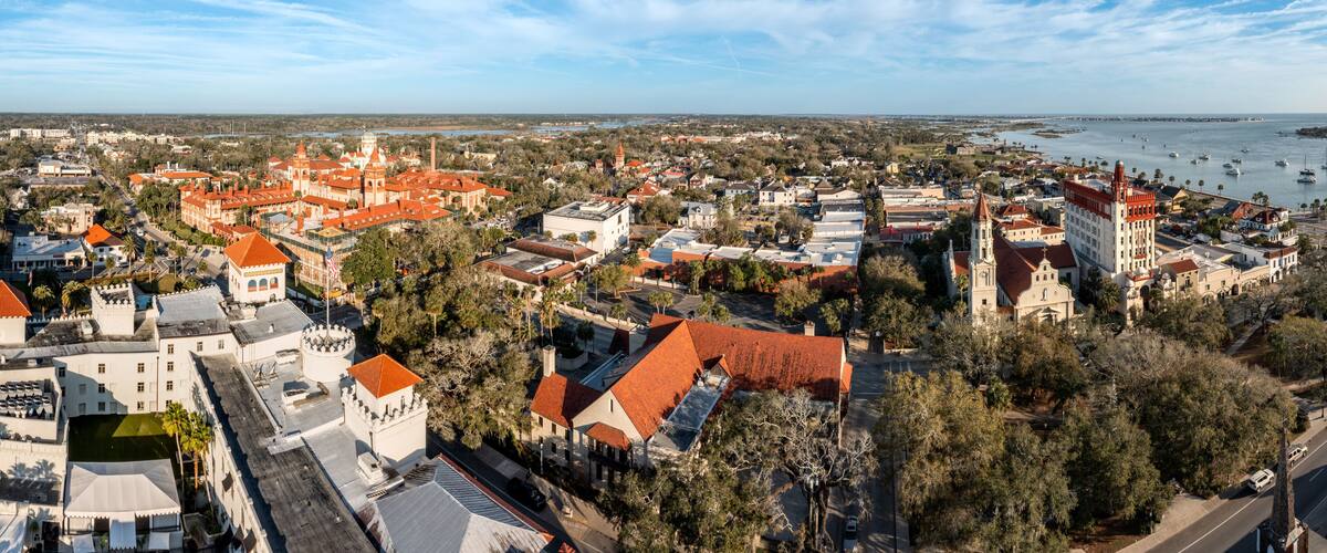 An aerial view of a coastal town with historic buildings, a prominent church, and a marina with boats.