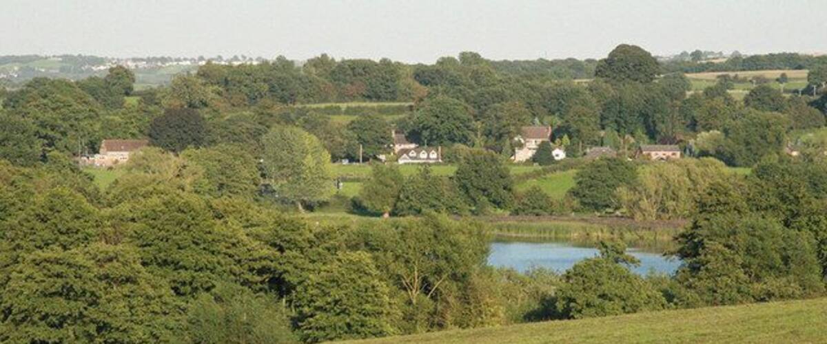 A rural landscape with rolling hills, a lake, and scattered houses.