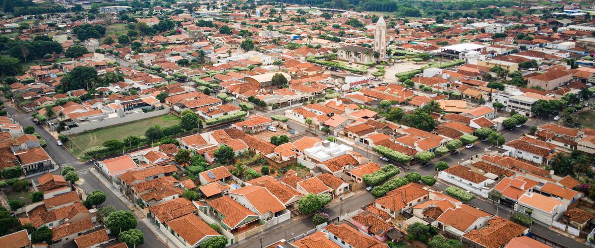 An aerial view of a town with red-tiled roofs, a prominent church tower, and surrounding green fields.