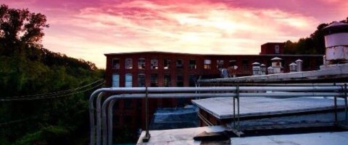 A rooftop with a metal railing overlooking a building and a sunset sky.