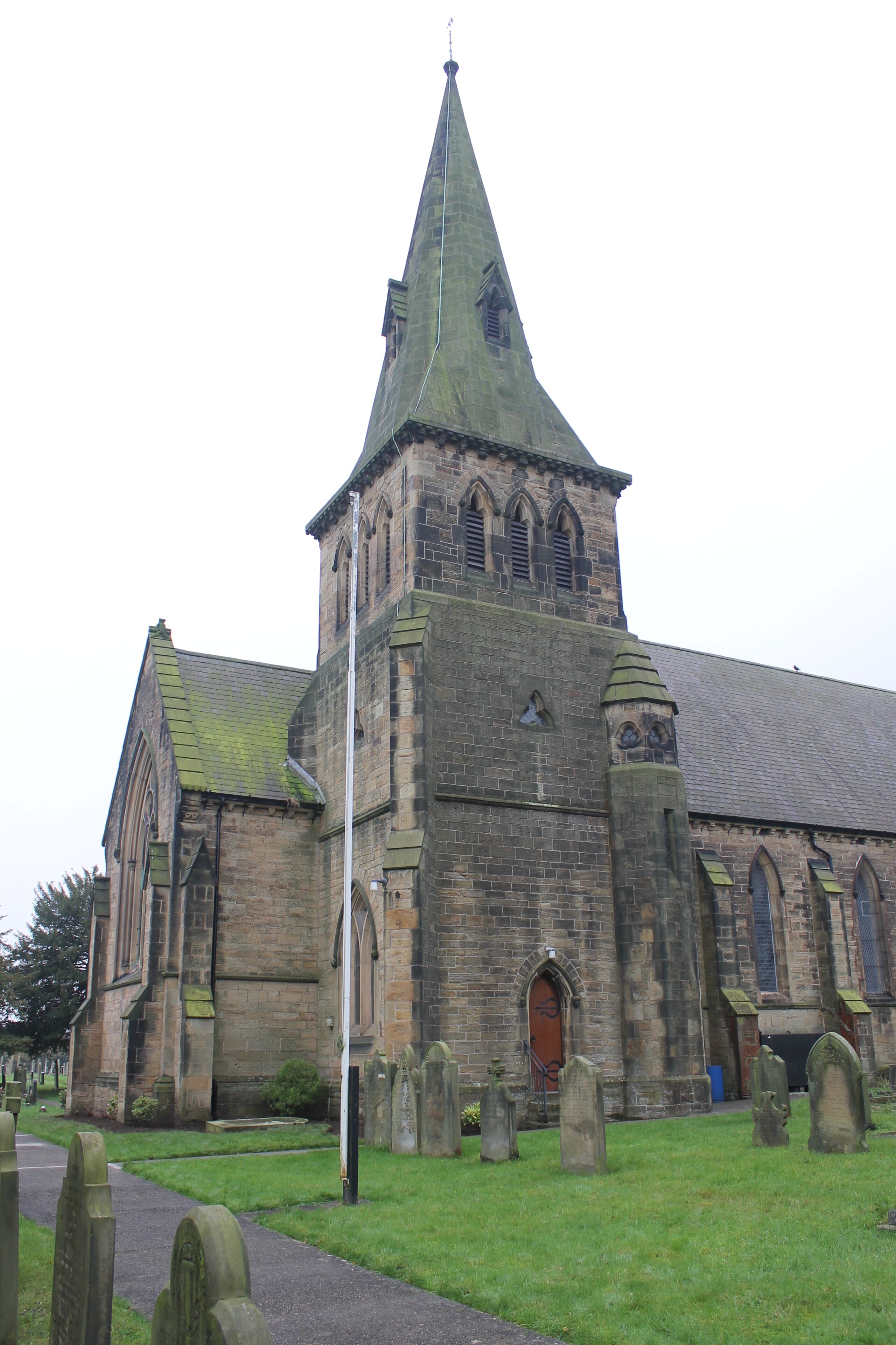A historic church with a tall spire and a graveyard in front.
