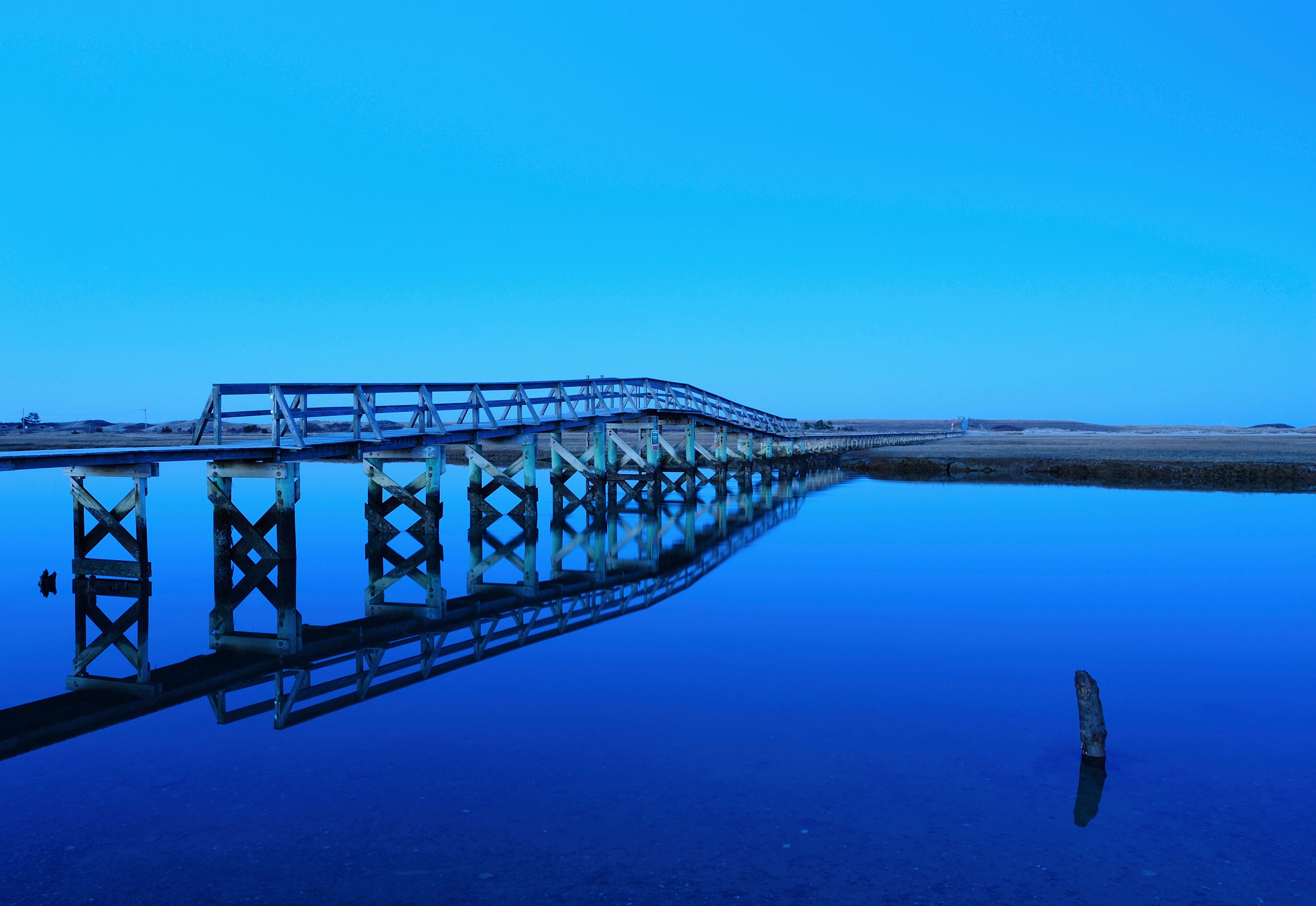 A long pier extending into a calm body of water with a clear blue sky above.
