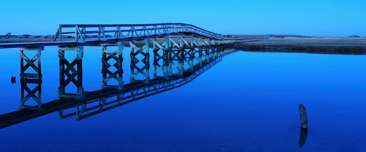 A long pier extending into a calm body of water with a clear blue sky above.