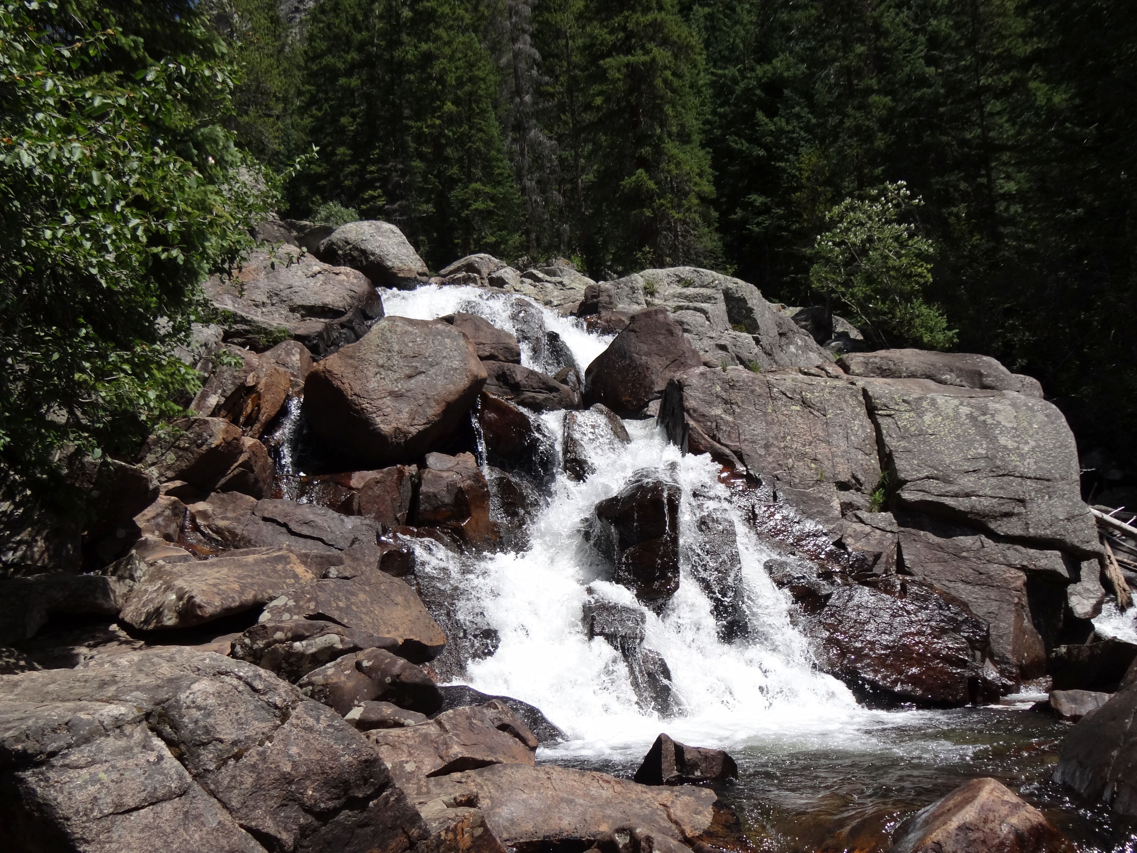 A waterfall cascading over large rocks in a forested area.