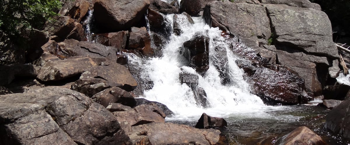 A waterfall cascading over large rocks in a forested area.