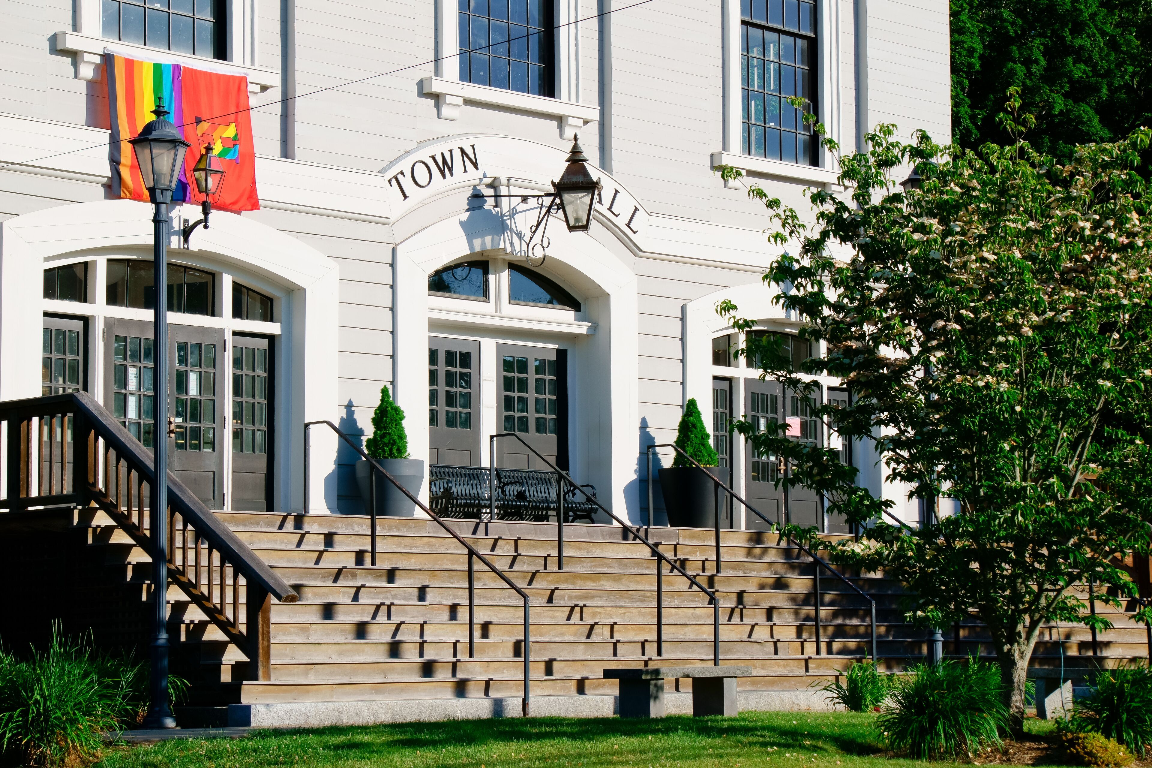 A white building with a sign reading "TOWN HALL" and a rainbow flag.