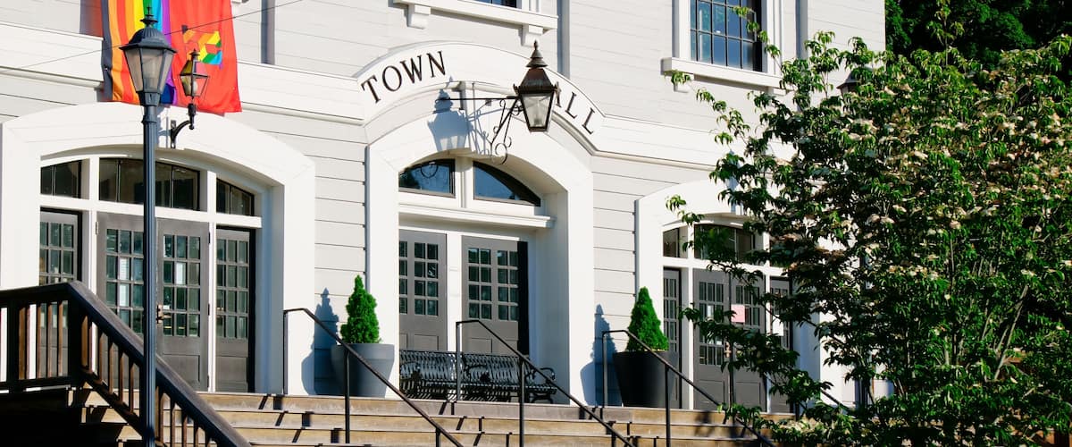 A white building with a sign reading "TOWN HALL" and a rainbow flag.