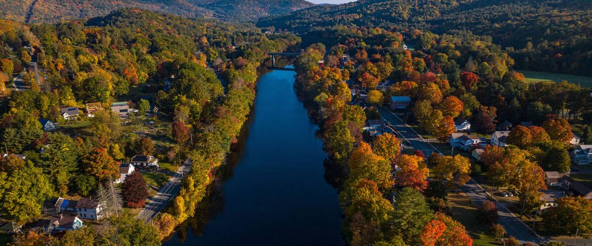 A river flanked by autumn-colored trees and residential areas.