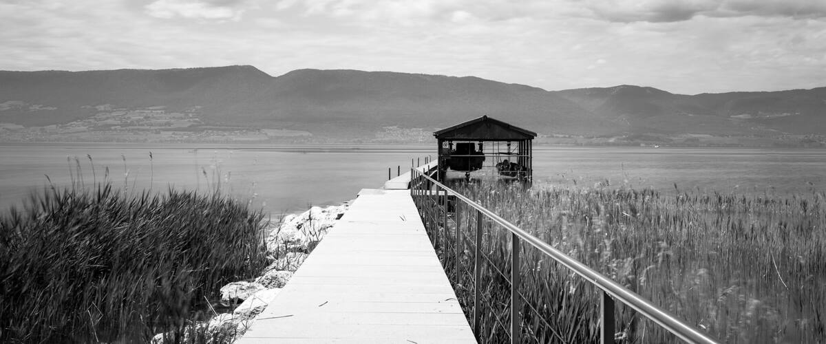 A wooden pier leading to a small wooden structure by a calm lake with mountains in the background.