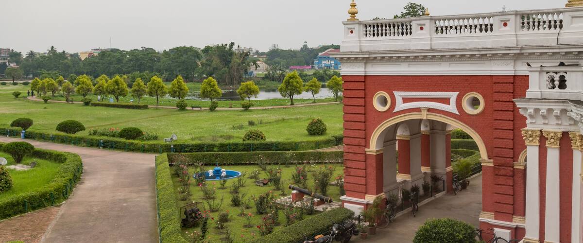 A large red and white archway with a fountain in a well-manicured garden.