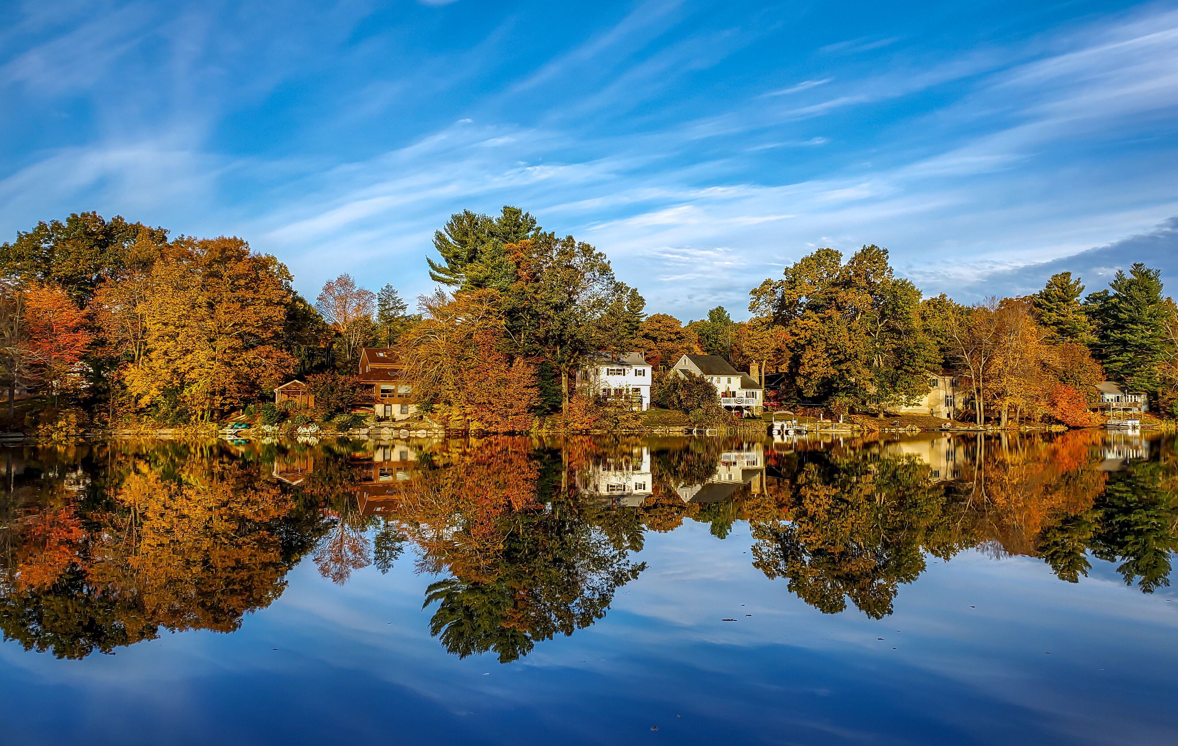 A serene lake with autumn-colored trees reflecting on the water, surrounded by houses.
