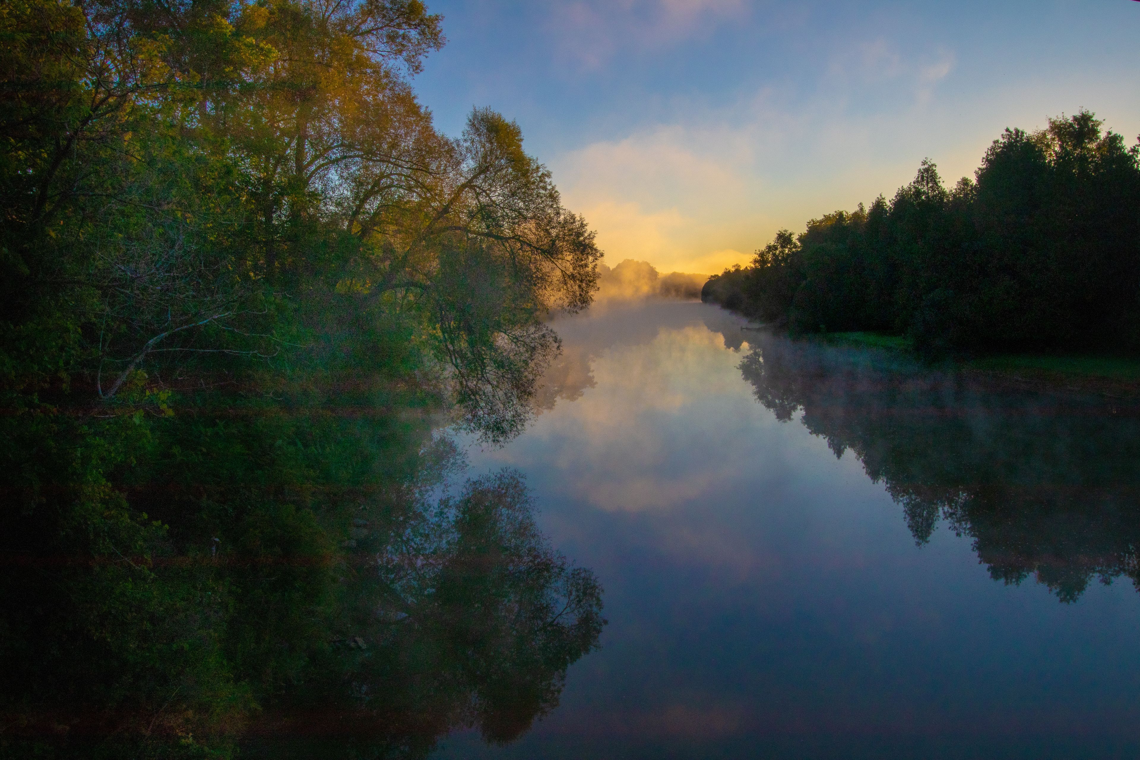 A calm river reflecting trees and a clear sky.