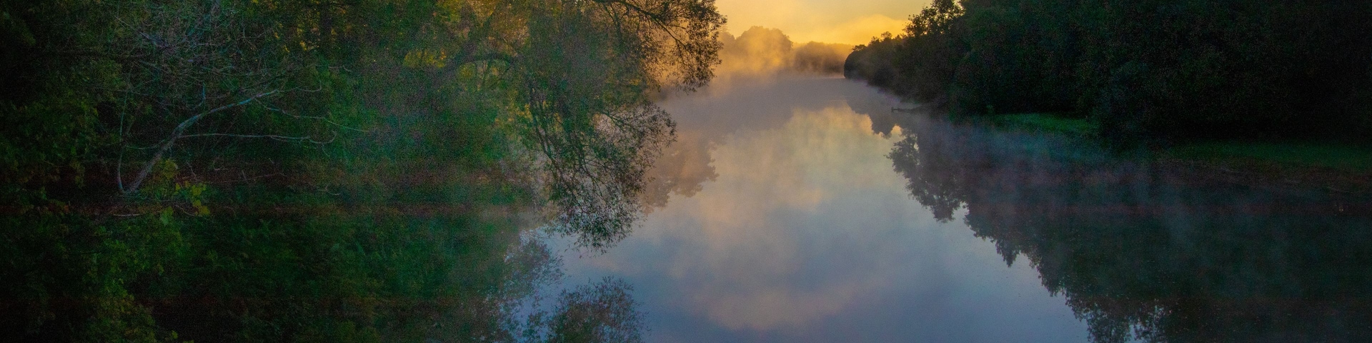 Um rio tranquilo refletindo árvores e um céu limpo.