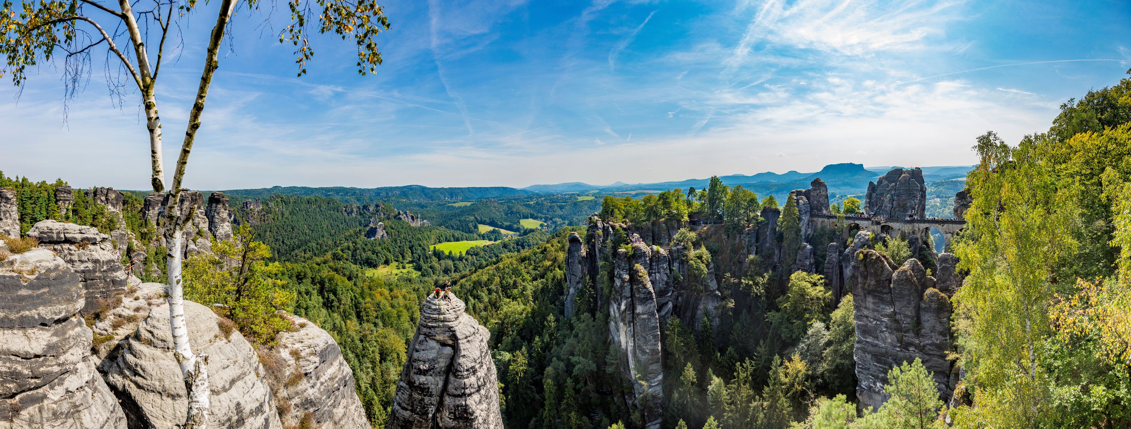 A landscape with rock formations, trees, and a distant view of a valley.