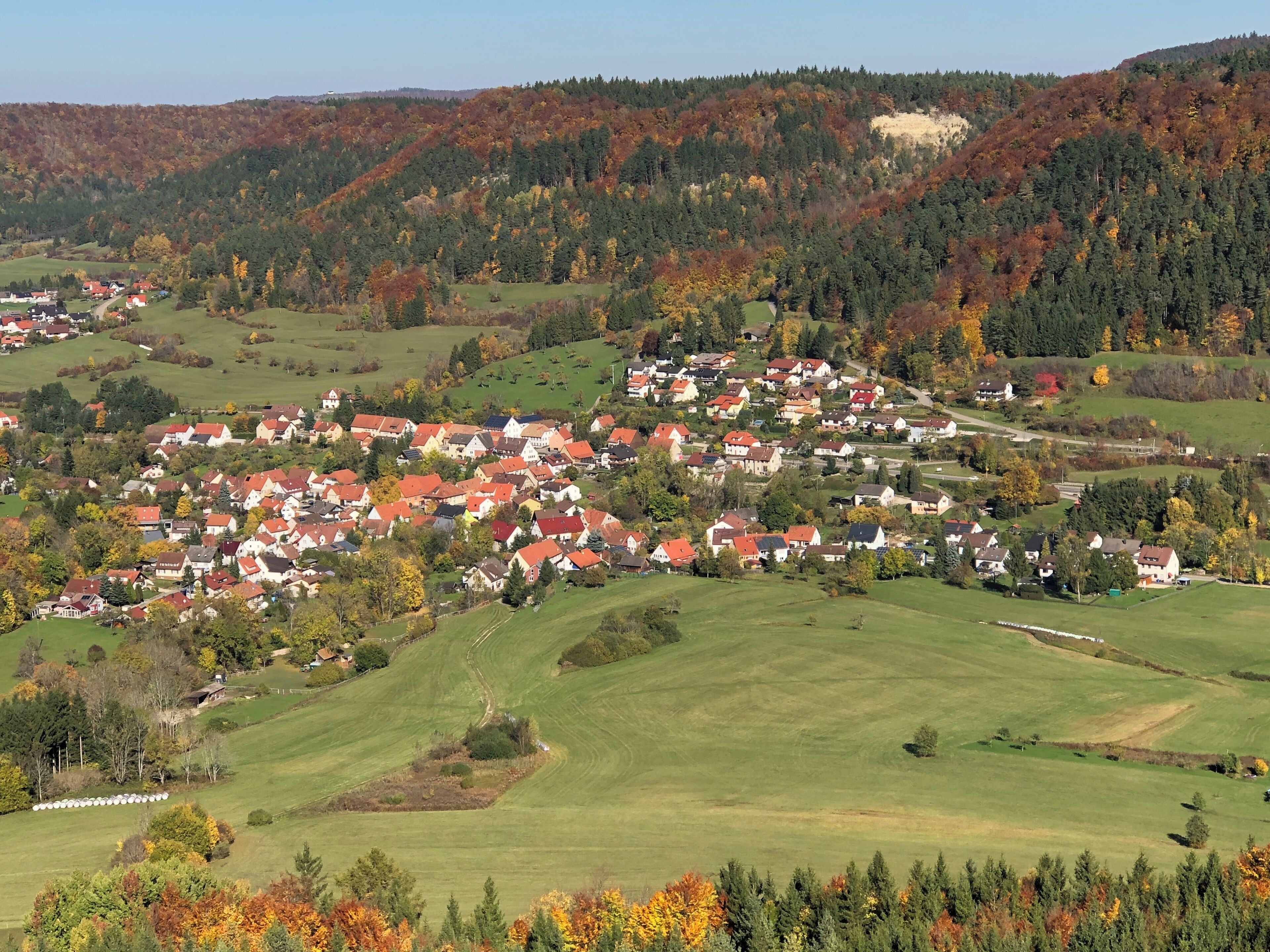 A rural village nestled in a valley with rolling hills and autumn-colored trees.