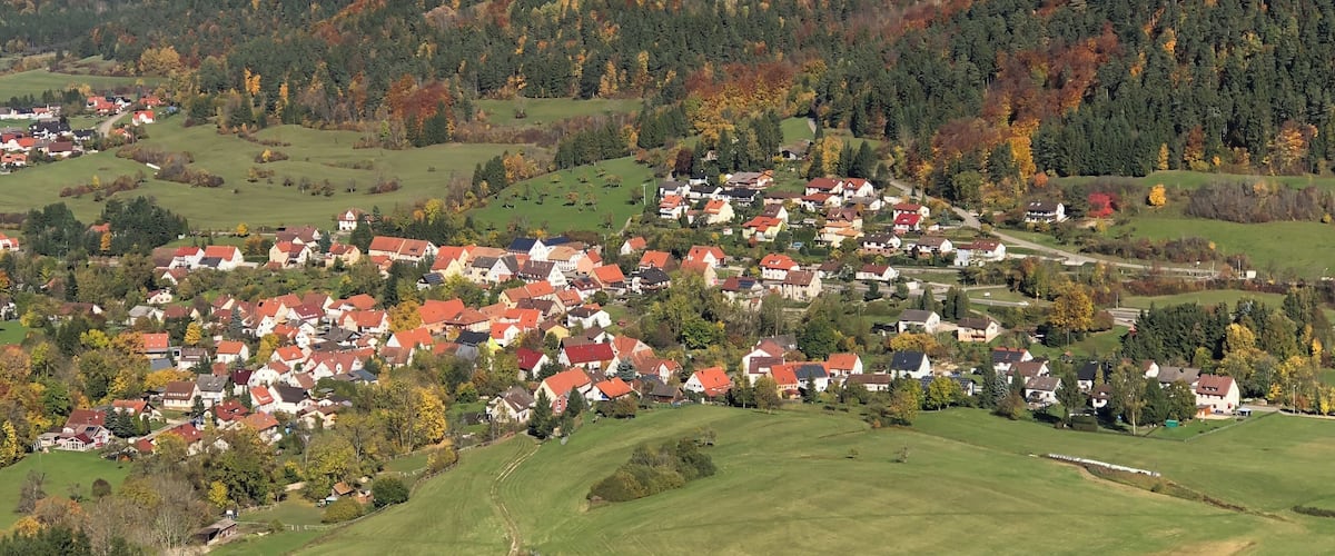 A rural village nestled in a valley with rolling hills and autumn-colored trees.