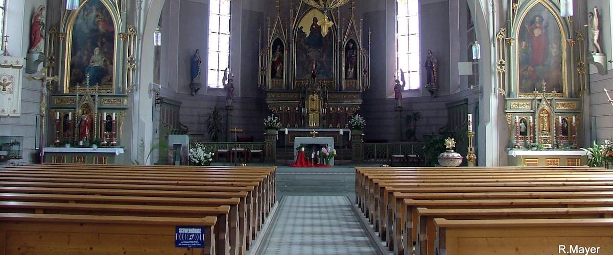 An ornate church interior with a large chandelier, arched windows, and religious paintings.