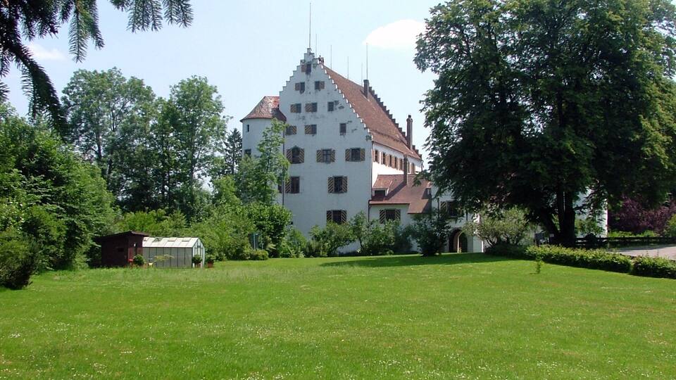 A large white building with a steep roof, surrounded by lush green grass and trees.