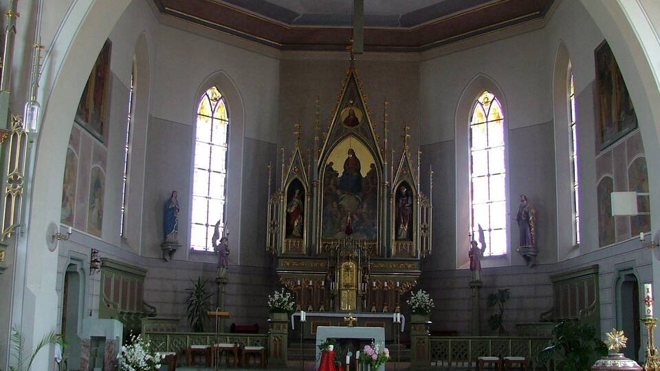 An ornate church interior with a central altar, stained glass windows, and religious statues.