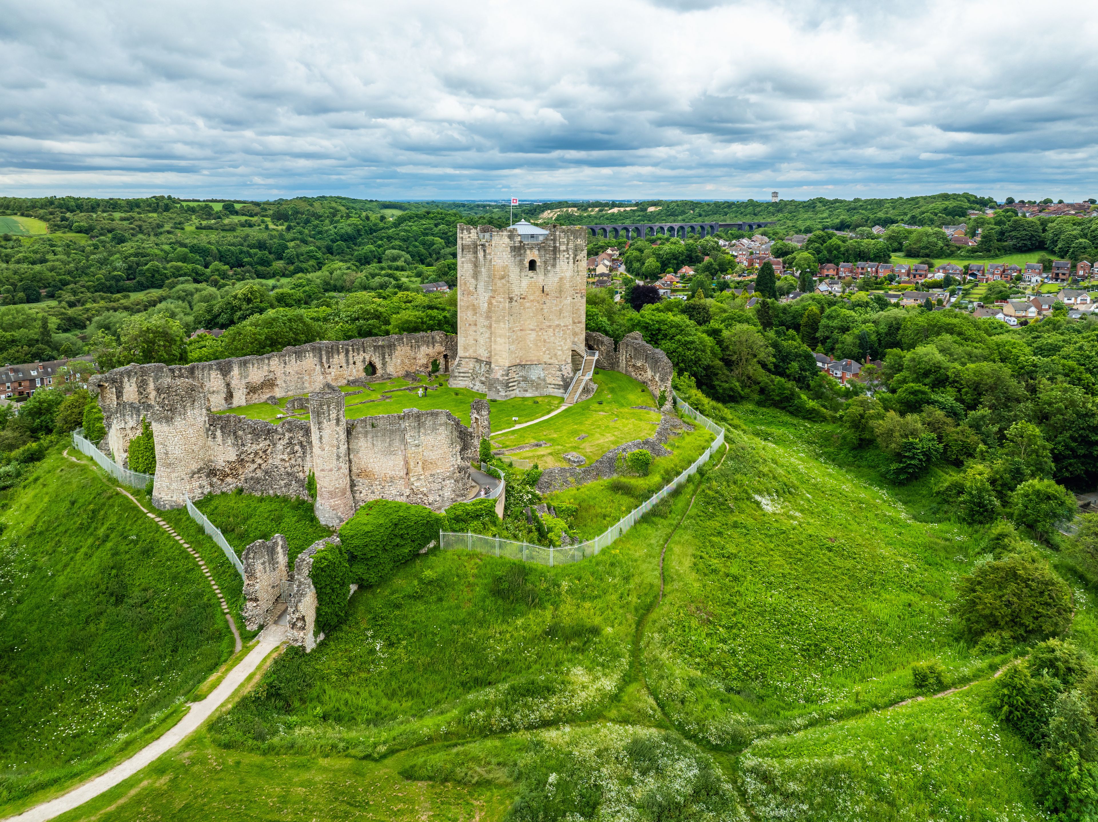 A historic castle surrounded by lush greenery and a small town in the background.