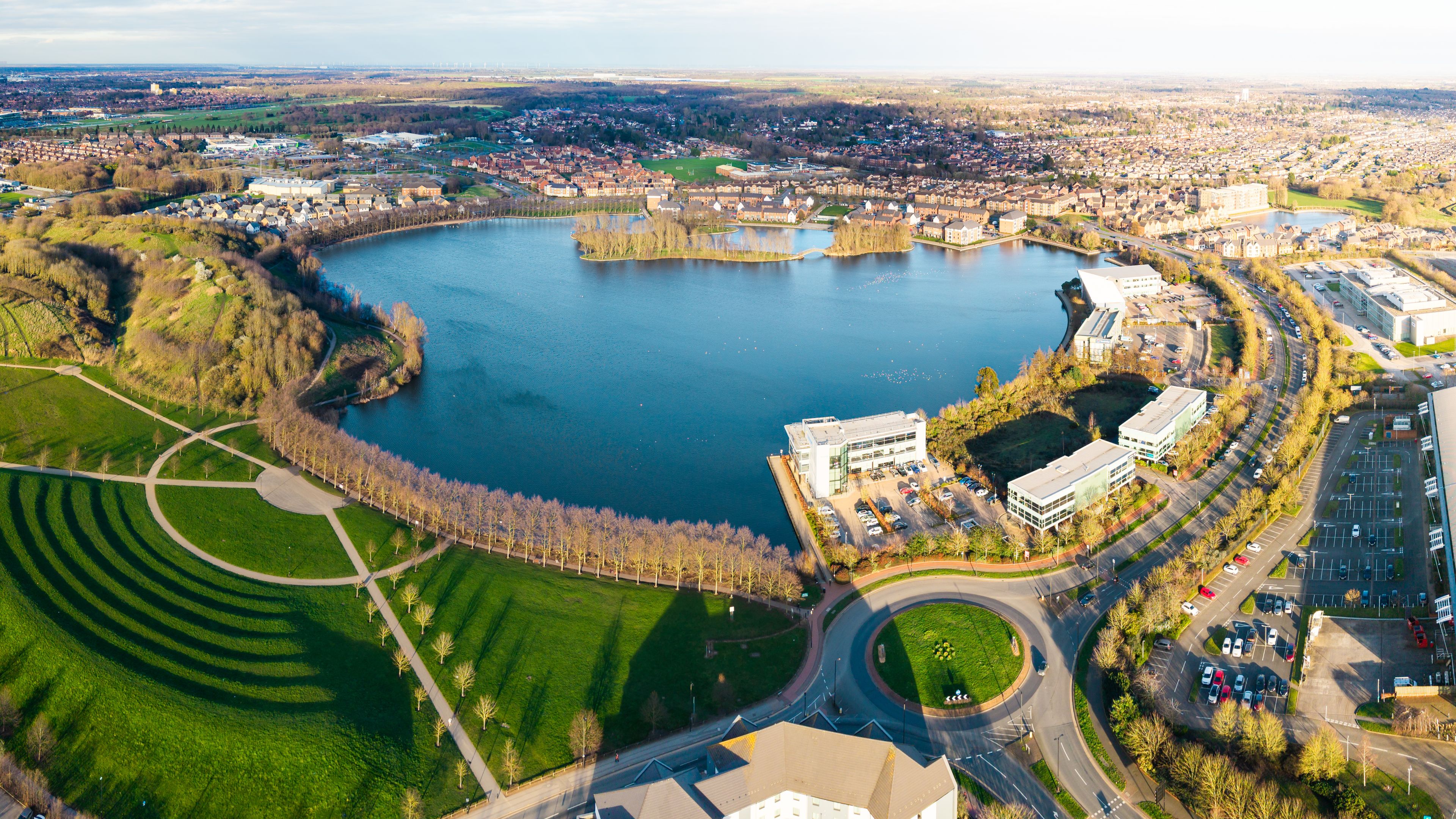 An aerial view of a city with a large lake, surrounding greenery, and modern buildings.