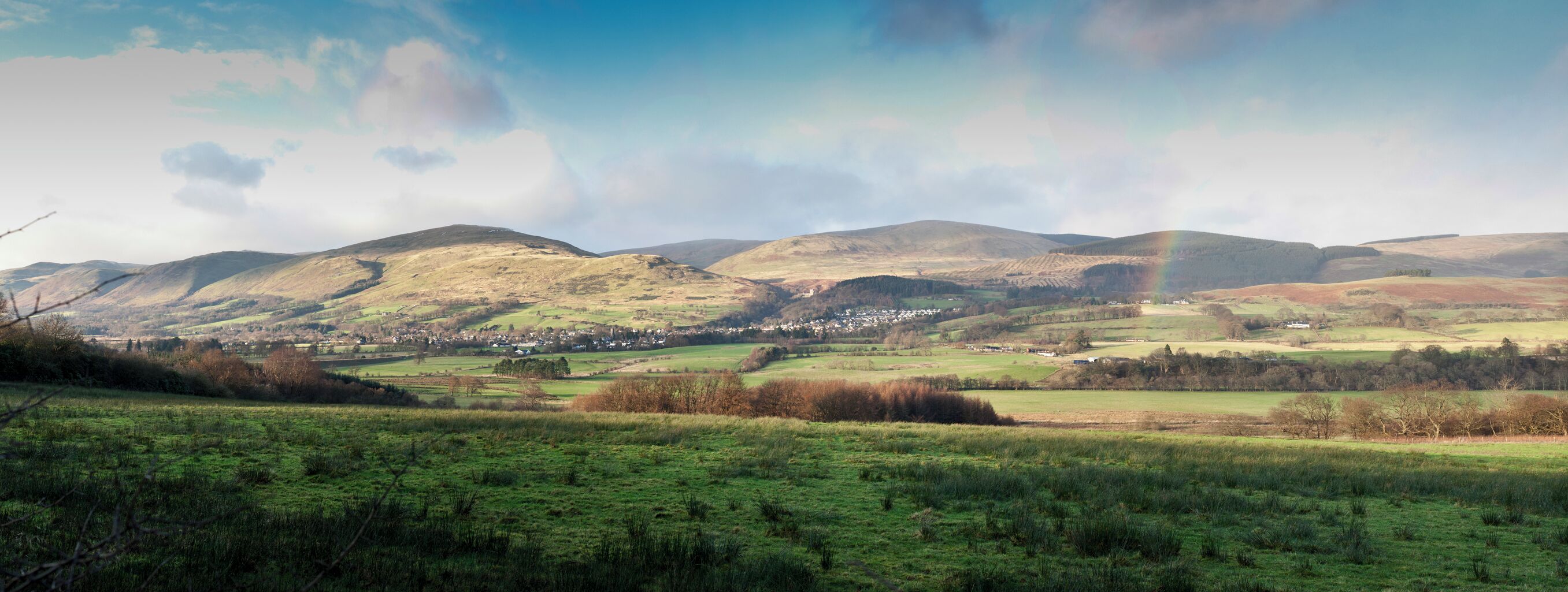 Rolling hills, a small village, and a rainbow in a rural landscape.