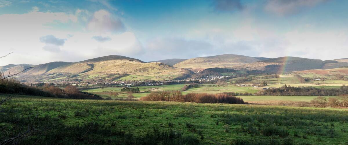 Rolling hills, a small village, and a rainbow in a rural landscape.