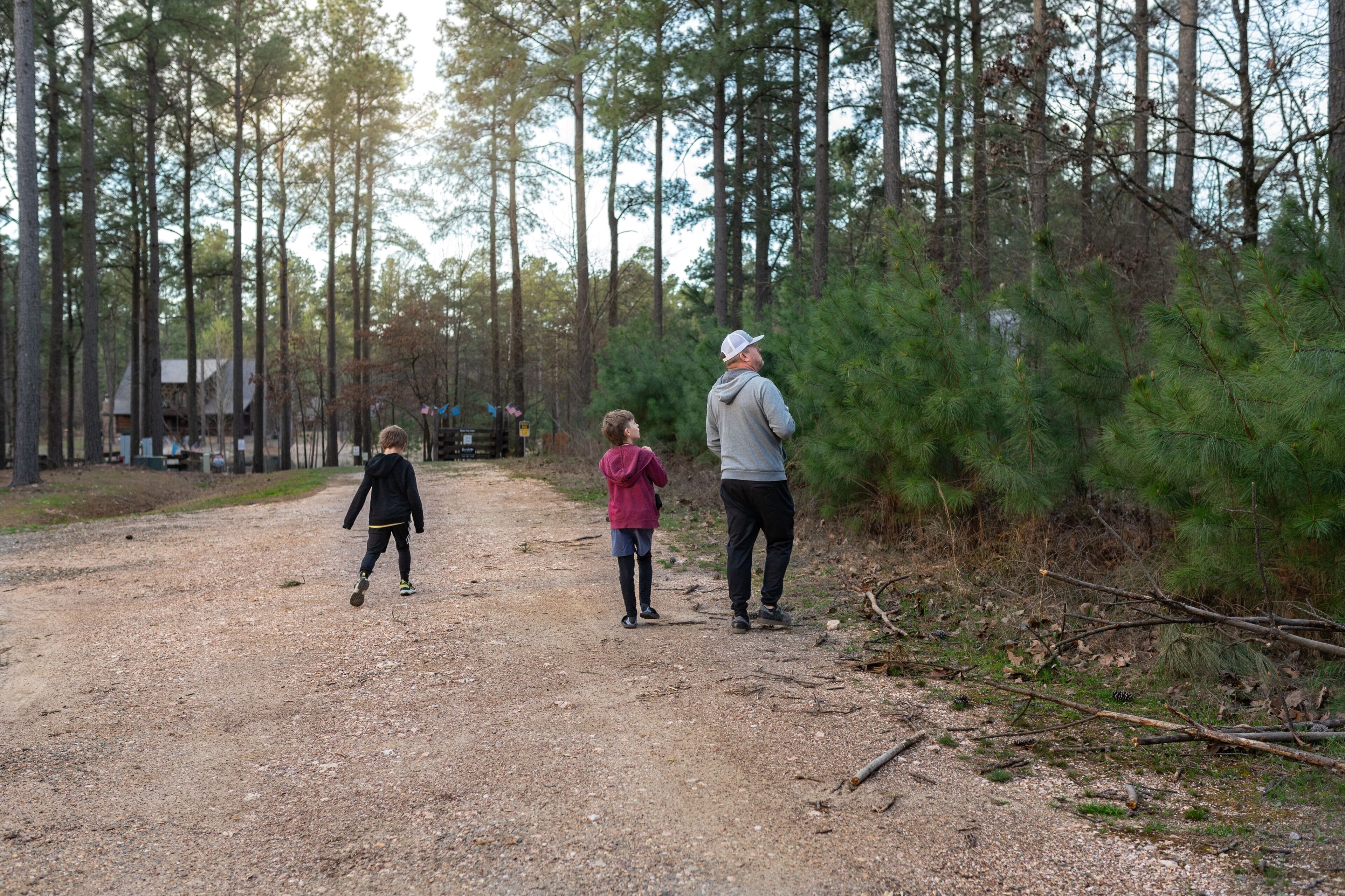 Dad and two kids walking a dirt path through a pine forest