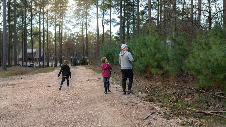 Dad and two kids walking a dirt path through a pine forest