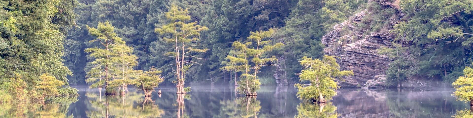 A calm lake surrounded by dense forest and rocky cliffs.