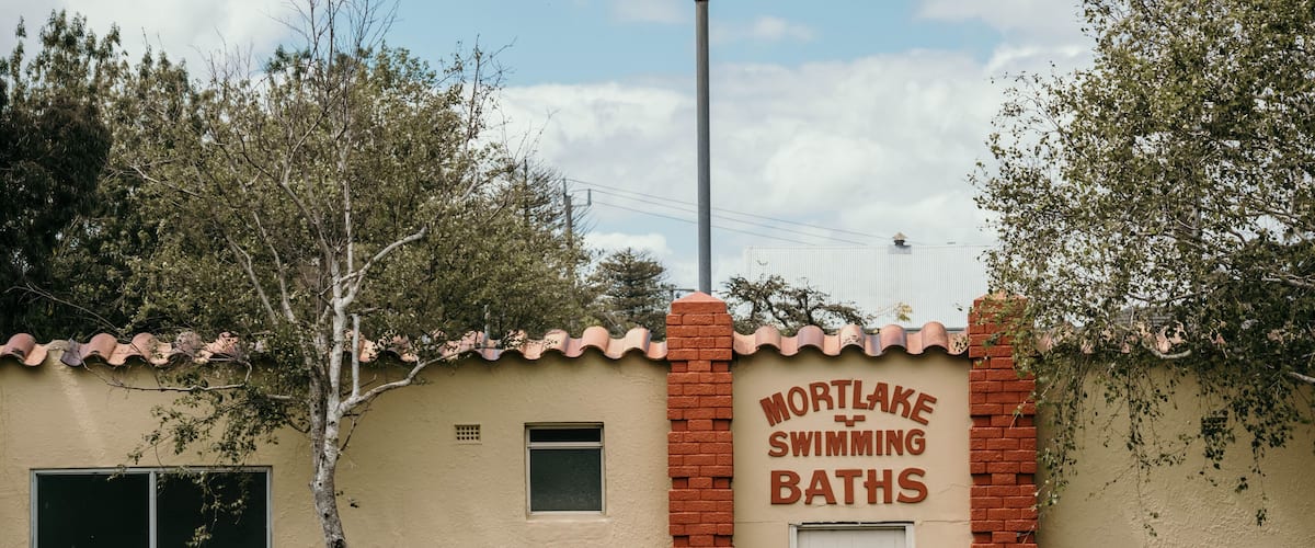 A building with a sign reading "Mortlake Swimming Baths" and a red brick entrance.