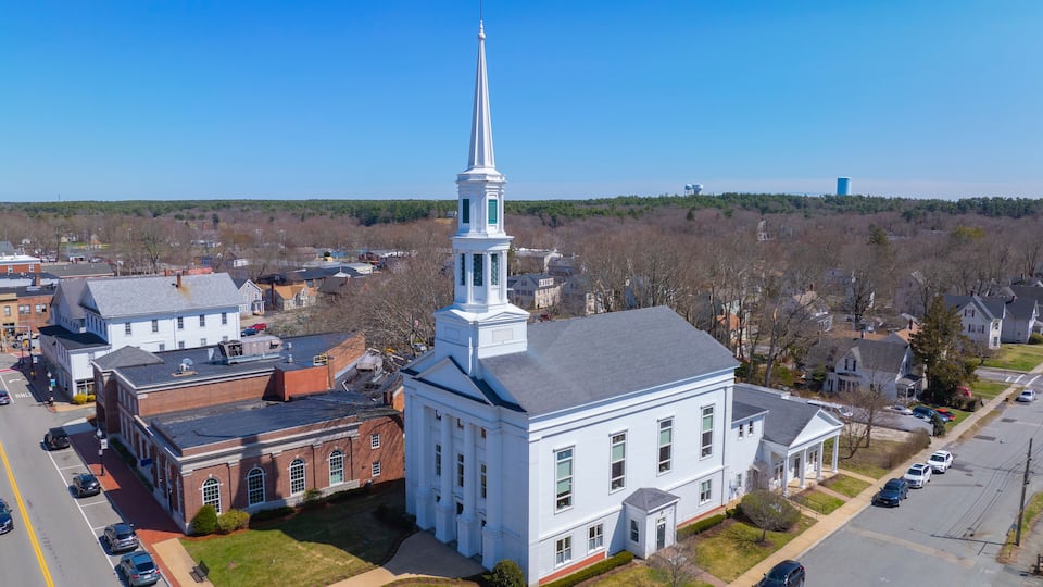 A church with a tall steeple, surrounded by residential buildings and a parking lot.