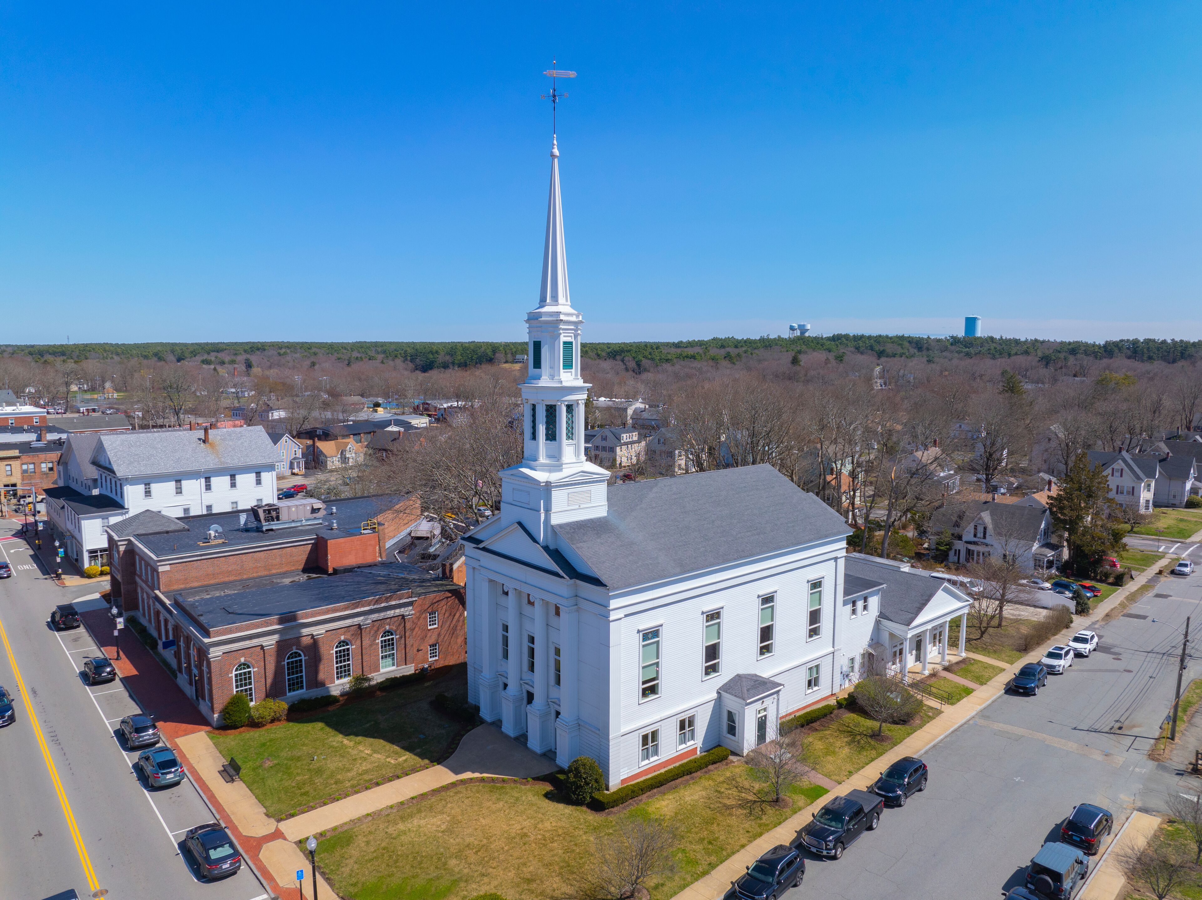 A church with a tall steeple, surrounded by residential buildings and a parking lot.